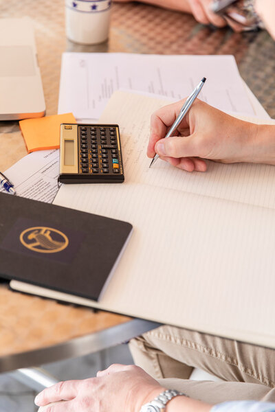 detail of consultat worhing with calculator, pen and notebook during a client meeting by laure photography