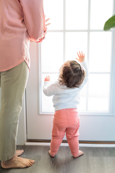 A baby gazing up at her grandmother during an intimate in-home photography session, framed by soft natural light from a window.