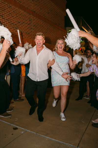 Husband and wife running at their wedding exit while their guest cheer them on.