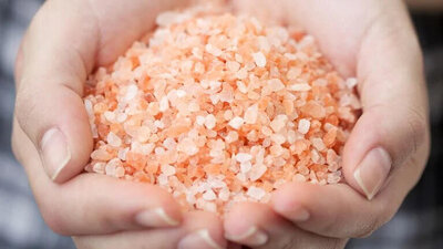 A close-up of two hands gently cupping a pile of pink Himalayan salt crystals, displaying their rough texture and varying shades of pink and white—often used in massage therapy sessions in Tolleson, Arizona.