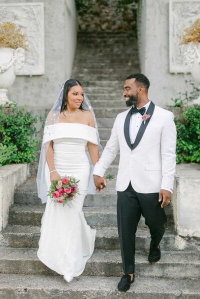 Elegant bride and groom holding hands on stone steps of a historic Italian villa — Destination Wedding Photographer Portfolio.