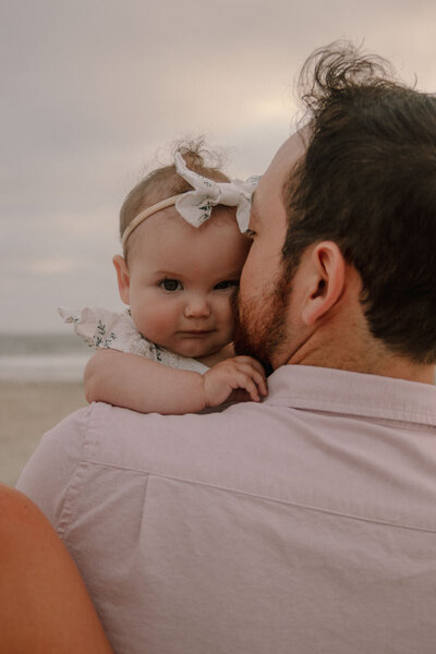 Baby girl looking over her father's shoulder at the beach