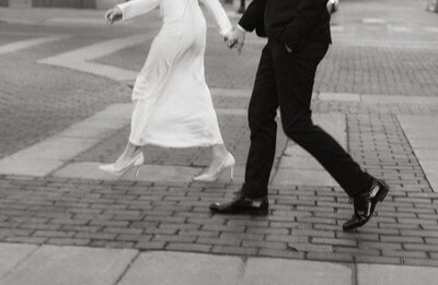 A stylish couple walking hand in hand through city streets, captured in a cinematic black and white frame.