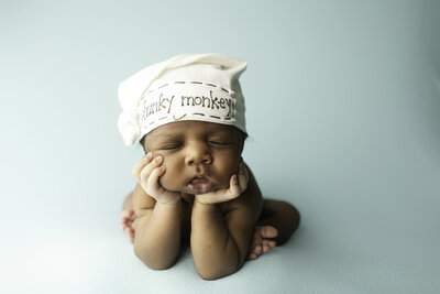 A serene newborn baby comfortably posed in the froggy pose, resting peacefully on a soft blanket with their chin resting on their tiny hands, beautifully captured in the studio by Chunky Monkey Photography