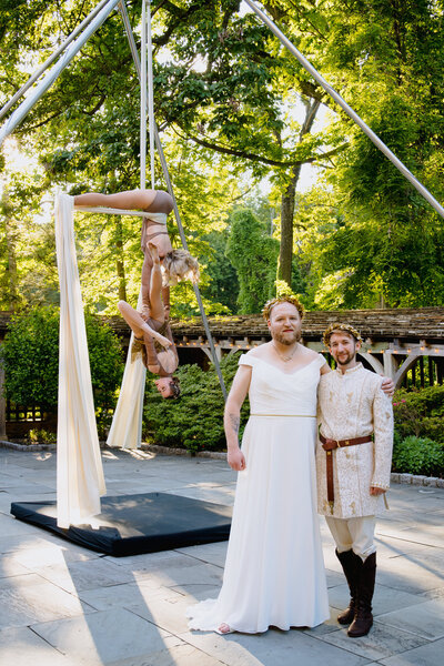 A wedding couple standing on a deck in a wooded area with a acrobat performer next to them.