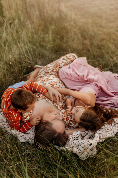 Lawrence Family Photographer captures mom with her two children laying on a lace blanket in a field at sunset
