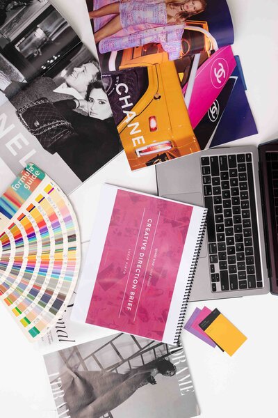 Professional brand strategy workspace with color fan deck, laptop, creative direction guide, and brand materials arranged on desk