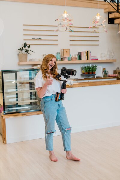 Iowa Brand Photographer stands with camera in coffee shop