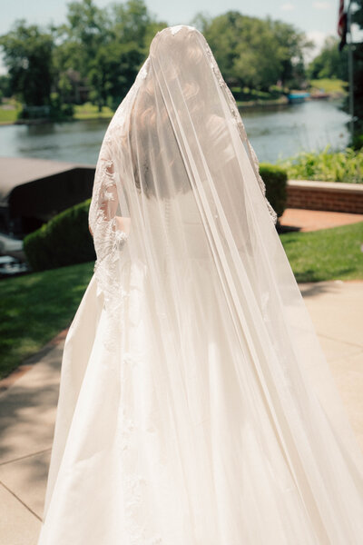 Bride walking toward waterfront patio with full veil and embroidered lace detail