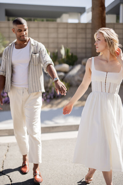 A carefree and romantic moment between a stylish couple strolling through the sunlit streets of Palm Springs, California. With effortless movement and soft golden light, this fine art image embodies the essence of love and timeless elegance in the desert.