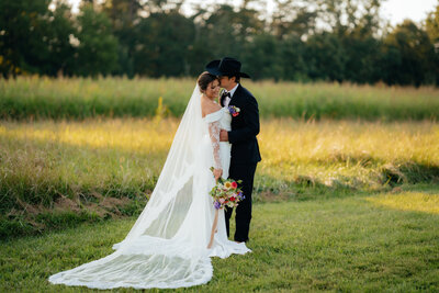 man wearing a cowboy hat kissing a woman while standing in a green field 