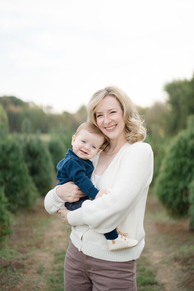 a-mom-holding-her-son-and-smiling-at-the-camera-for-christmas-tree-mini-portraits-with-nashville-family-photographer-dolly-delong