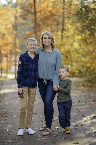 Mother with her two sons smile at the camera with the beautiful fall foliage in the background. Family photos by Amanda Touchstone