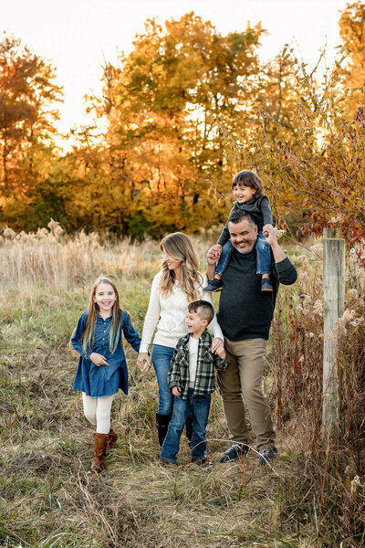 Family of five standing in the fall foliage laughing and smiling at each other.