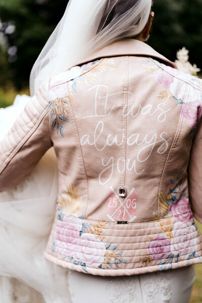 Guest in a pastel floral jacket with It was always you and a wedding date hand-painted on the back, attending an elegant Italian destination wedding.