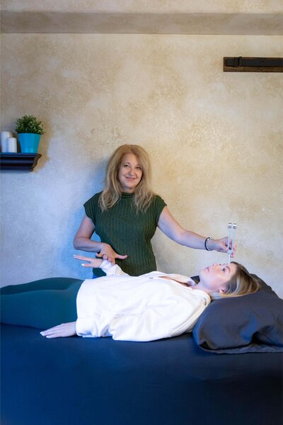 Cyndi Stewart performs an kinesiology session on a client using tuning forks in a peaceful, softly lit space.