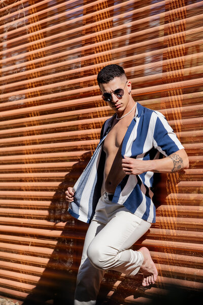 Sun-kissed and effortlessly stylish, this bold fashion moment in Palm Springs captures confidence and charisma. The striking striped shirt, crisp white pants, and retro shades set against the warm, textured backdrop create a modern yet timeless aesthetic.
