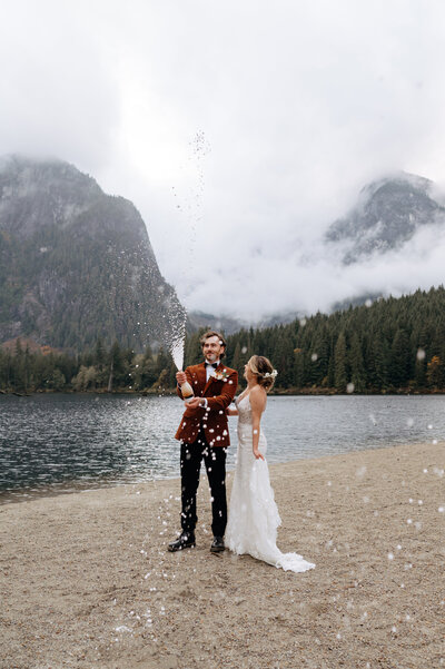 Adventure elopement with a couple beside an alpine lake opening a bottle of champagne