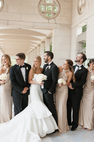 Bridal party in black tuxes and blush dresses looking at each other at the Muny in St. Louis