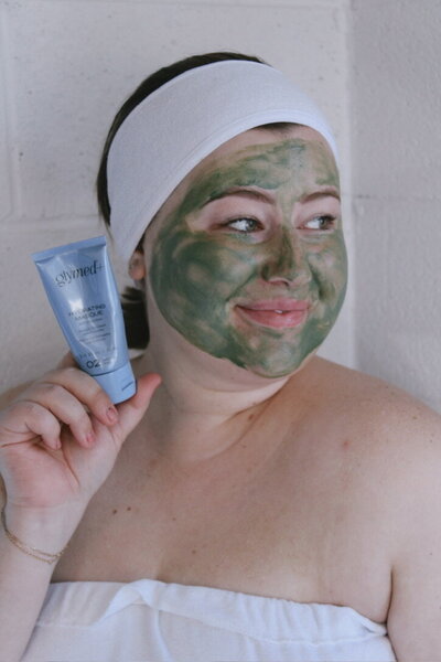 The owner of Syked about Beauty is giving one of her clients a facial with a big smile on her face