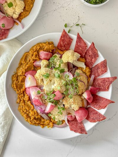 A bowl of golden beet purée with roasted cauliflower, radishes and turkey bacon.