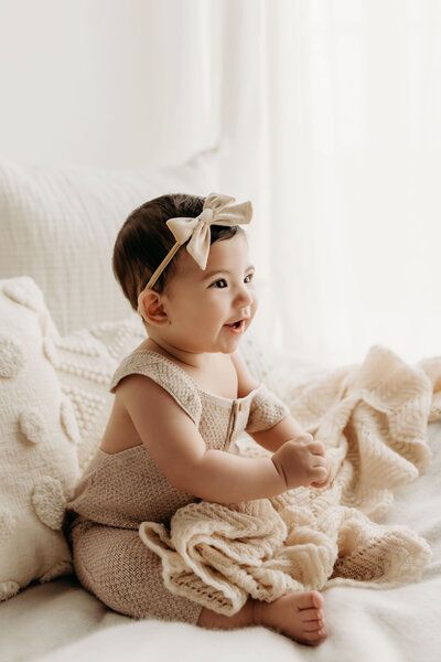 A six month old baby sits proudly amongst neutral knits and blankets in a natural light studio in Vancouver Washington