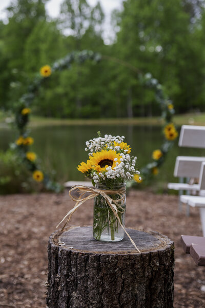 sunflowers in a mason jar sitting on top of a tree stump