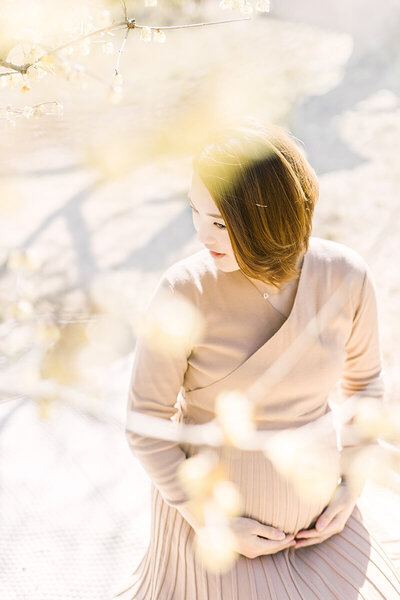 蠟梅の花の下でうつむきながら大きなおなかに手を添えた美しいマタニティフォト。