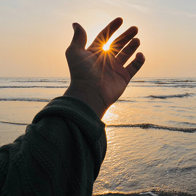 outstretched hand with sun shining between fingers