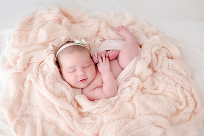 Newborn baby girl with a flower headband on a soft peach blanket