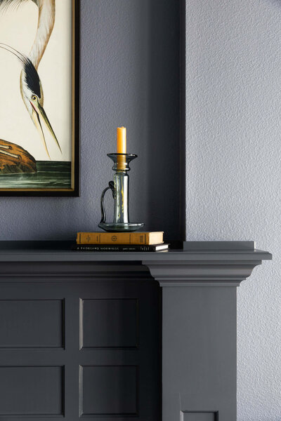 Close up of maple millwork shelf with books and a candle holder sitting on top of it and a peek of a heron painting.