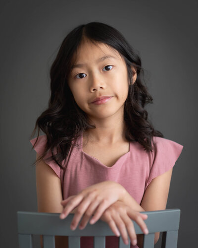 beautiful portrait of child in mauve dress with hands draped over backwards chair