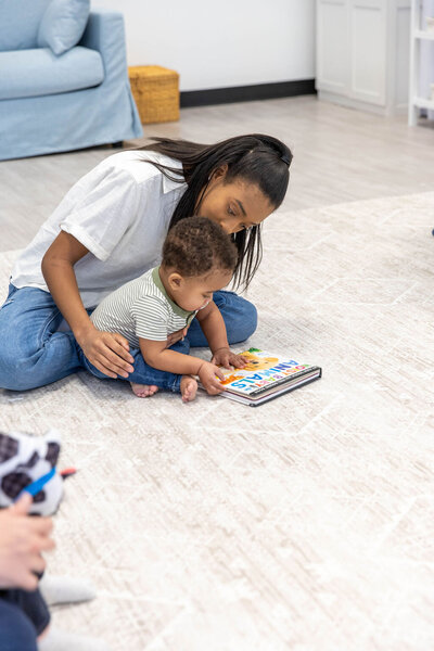 Woman holding her baby as he plays with a book