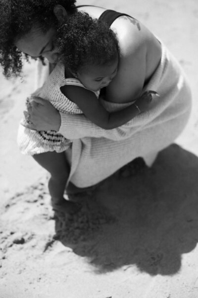 Woman hugging her toddler as they play on the beach