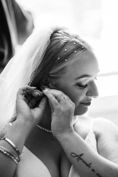 A stunning black and white photo of the bride looking down her arm while putting in her earrings