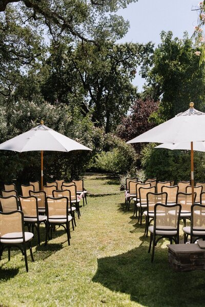 boise idaho photography of Elegant backyard wedding ceremony setup in an orchard with rattan and black chairs under white umbrellas