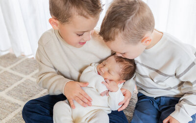 two young boys are holding their new baby brother and one brother is kissing the baby on the head