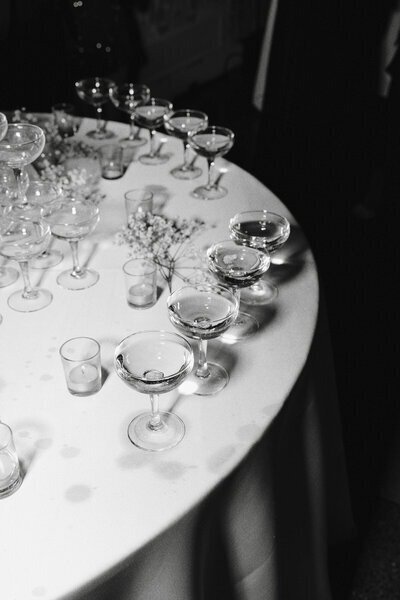 black and white image of a table at a wedding reception with glasses of wine or champagne shot by minnesota wedding photographers tom thornton photography