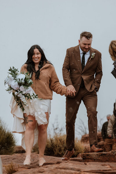 bride and groom holding hands and smiling while walking through the desert