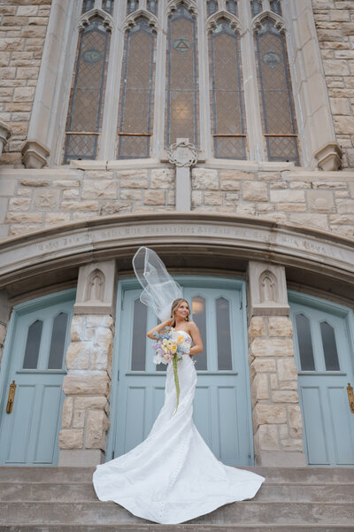 Bride stands in front of the blue doors and stairs at Melrose Abbey - a KC Wedding Venue. Photo by Anna Brace, a KC Wedding Photographer.