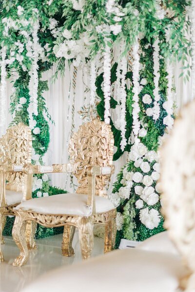 Elegant wedding venue decorated with white flowers and green foliage, featuring ornate golden chairs.