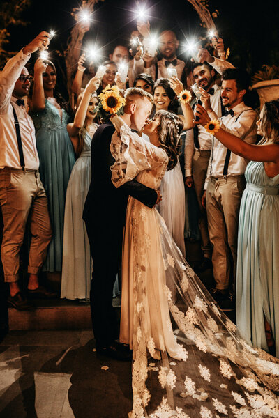 Happy couple kissing with other people cheering with phone flashlights