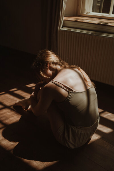 Een danseres die voorover gebogen in de lichtstralen van de zon zit