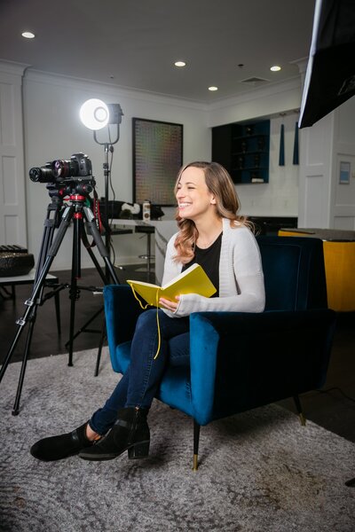 Woman videographer on video production set holding notebook and smiling to someone off camera