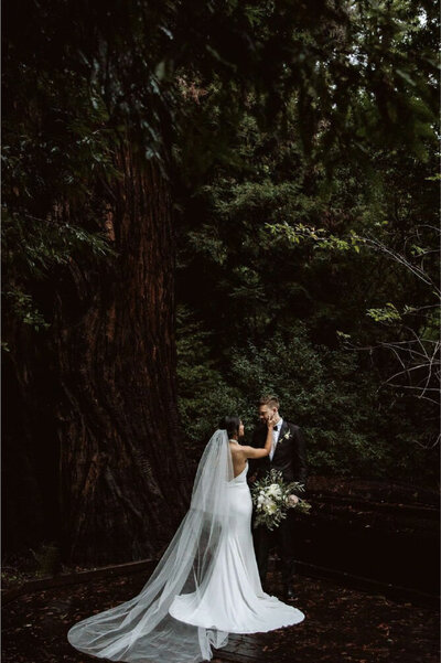 bride holding grooms face in woods