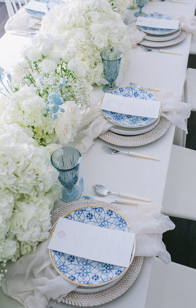 Spanish inspired table set with white and blue dinner plates, glasses and printed dinner menus