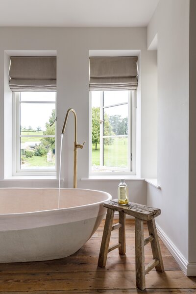 a cotswold bathroom with bath and antique stool overlooking the countryside