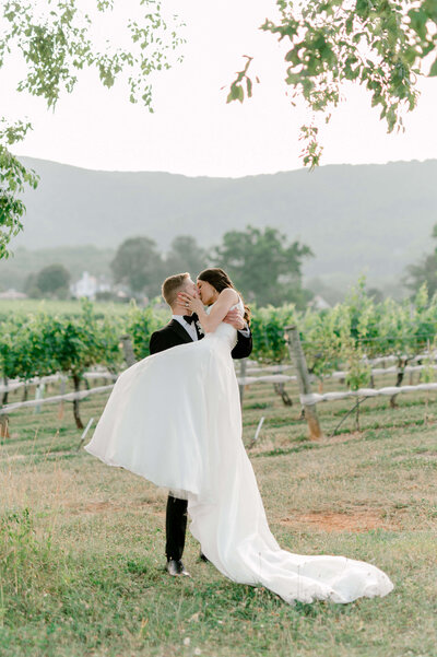 Romantic photo of groom picking up bride in a vineyard and kissing her, taken by DC wedding photographer, Rachael Mattio.