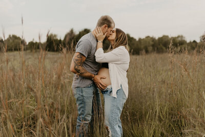 maternity photoshoot with woman kissing  in field