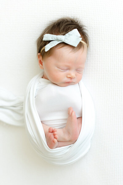 Swaddled baby girl with feet out and bow on head